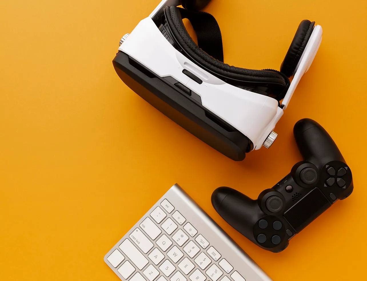 Custom game development concept with VR headset, game controller, and keyboard on yellow background